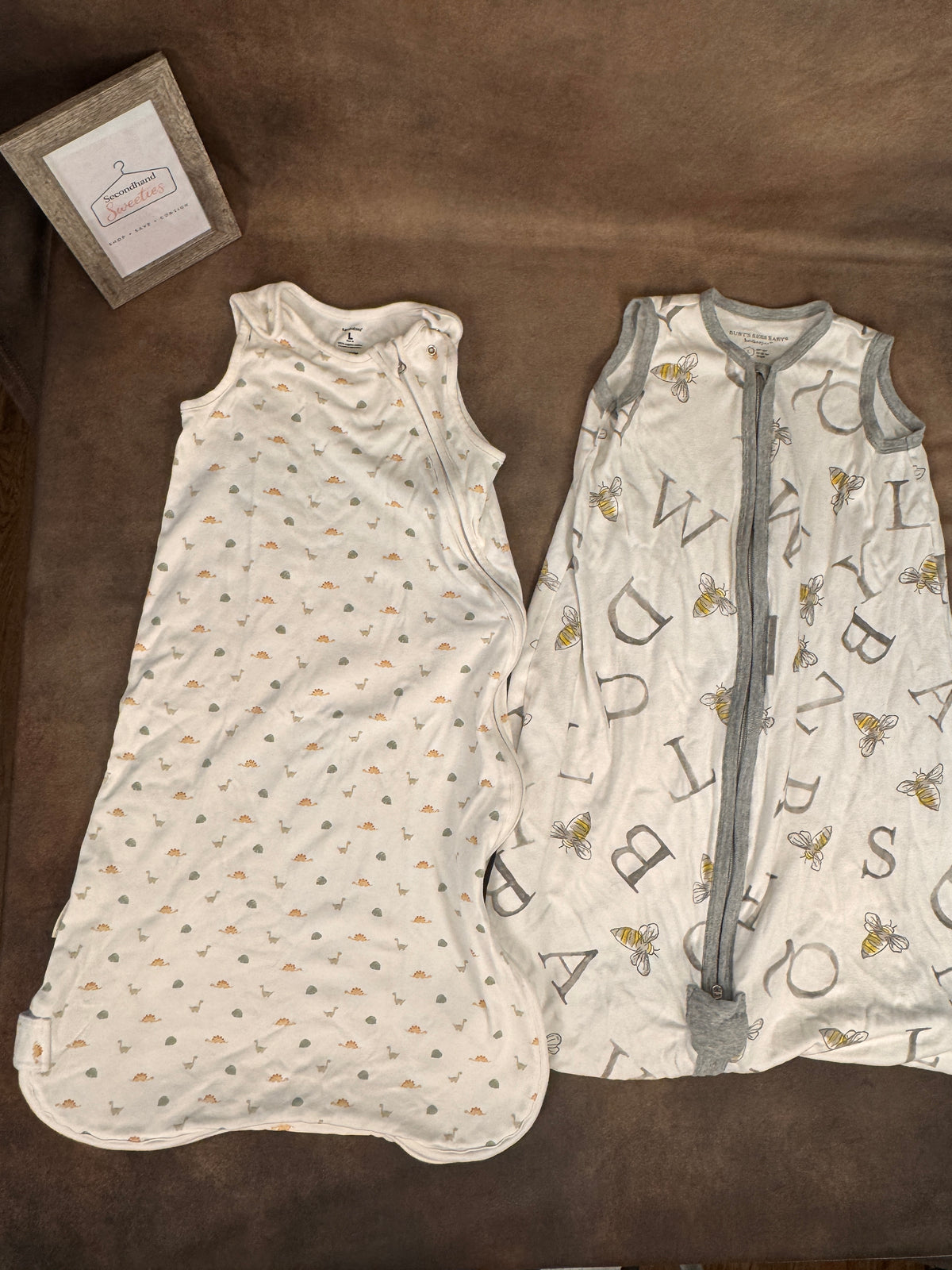 Two baby sleep sacks laid flat on a brown fabric surface. The left sleep sack is off-white with tiny scattered orange, gray, and black motifs.